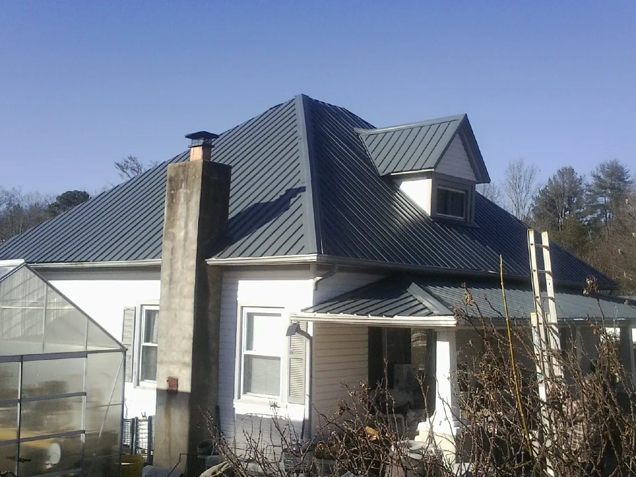 Dark blue standing seam metal roof on a white farmhouse with dormer — Slate & Tile Roof Repair by Roofing Brothers in Ohio City