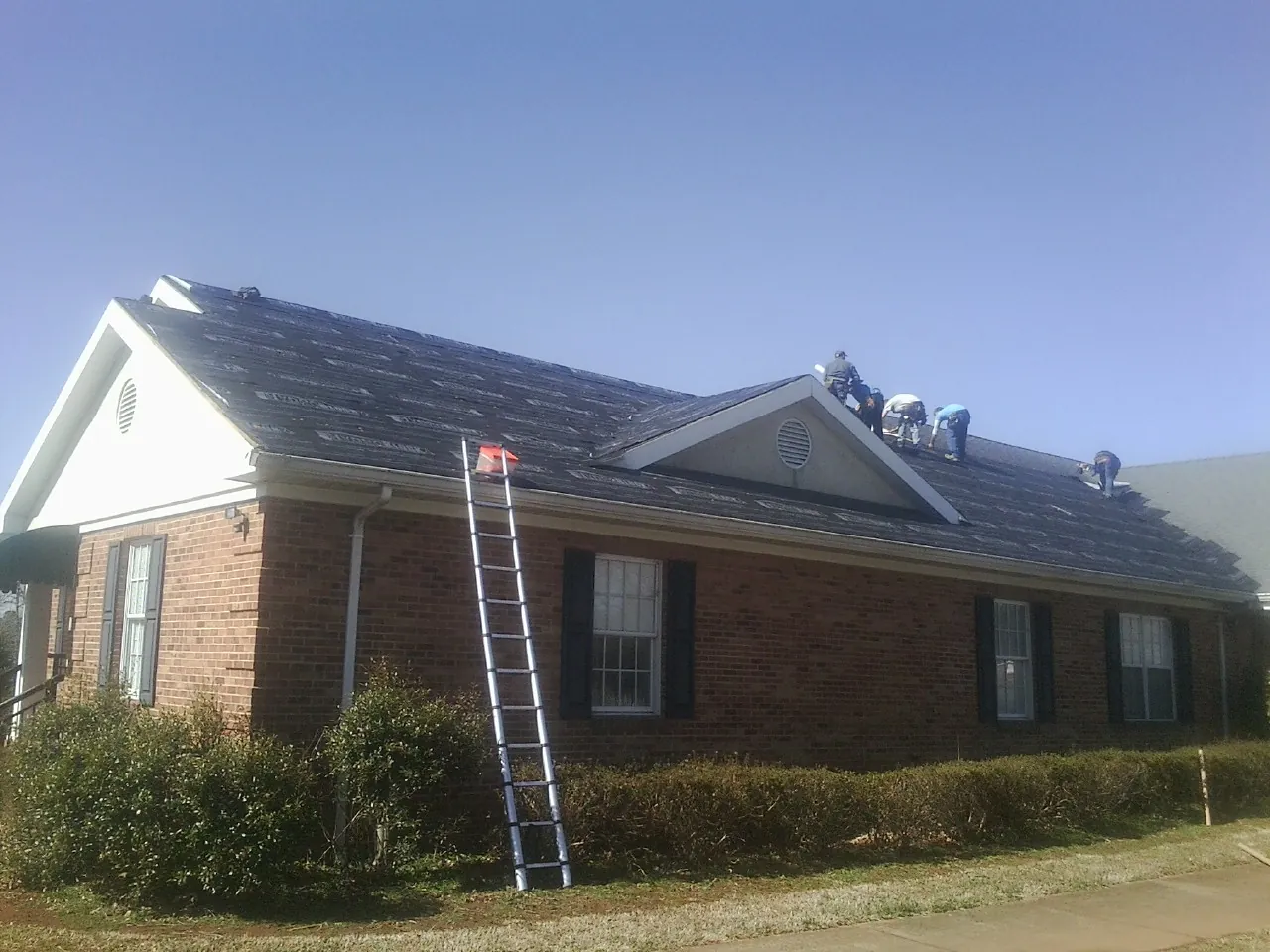 Crew tearing shingles off a brick ranch roof with a ladder set — Emergency Roof Repair work by our crew in Ohio City
