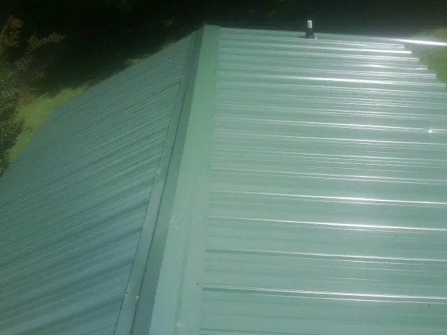 New green metal panels meeting at the ridge of a roof — Flat Roof Repair work by our crew in Ohio City