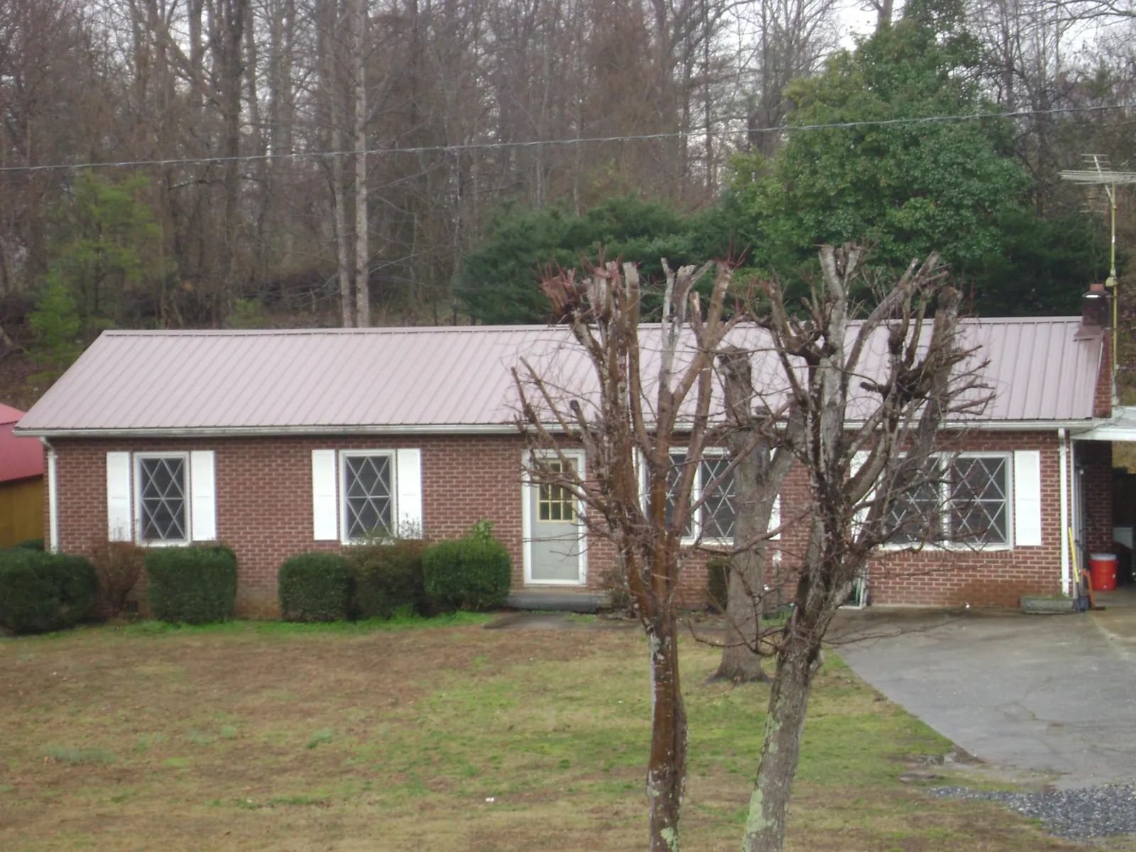 Mauve metal roof on a brick ranch home behind bare trees in Ohio City